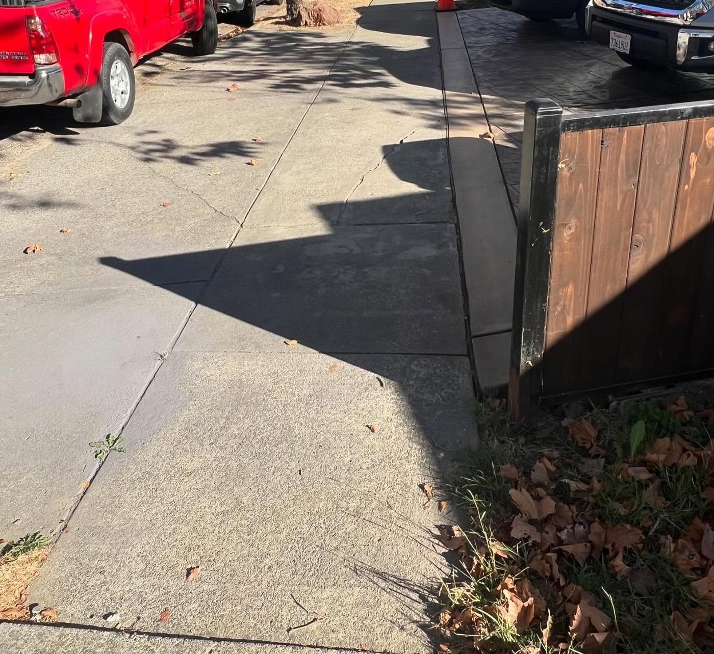 An old residential sidewalk beside a wooden fence, before the work